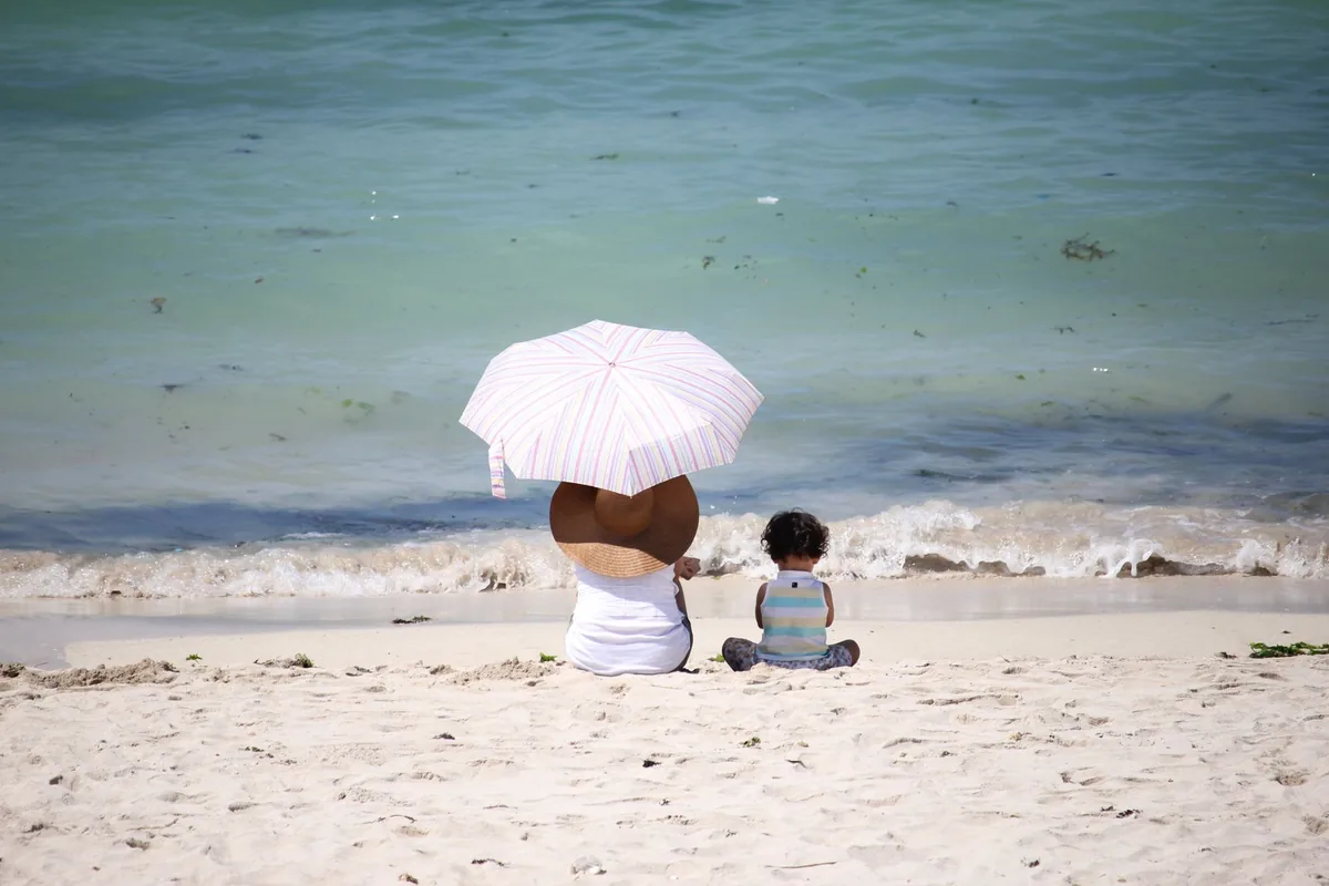 Mother and child sitting by the seaside, enjoying the sunny beach under an umbrella